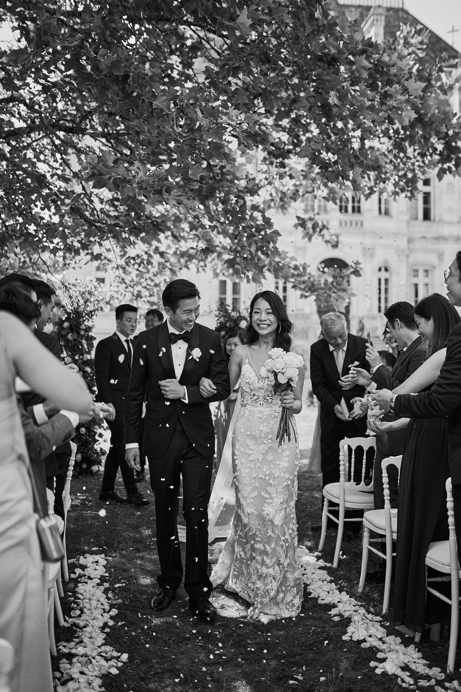 storybook europe wedding photographer Newly wedded couple doing an exit being showered with flowers in black and white with French chateau in the background