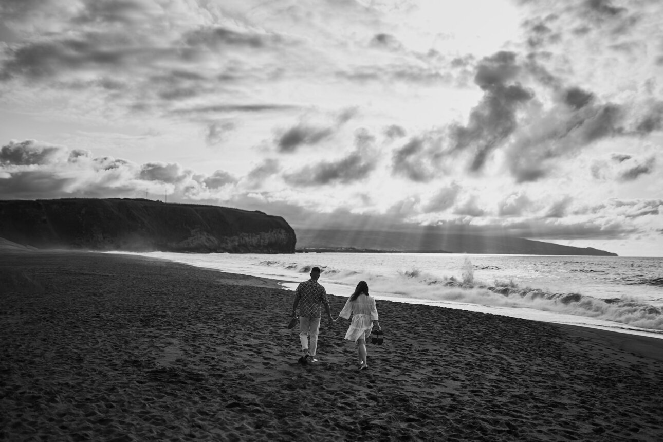 A couple walking on the beach under cloudy skies.